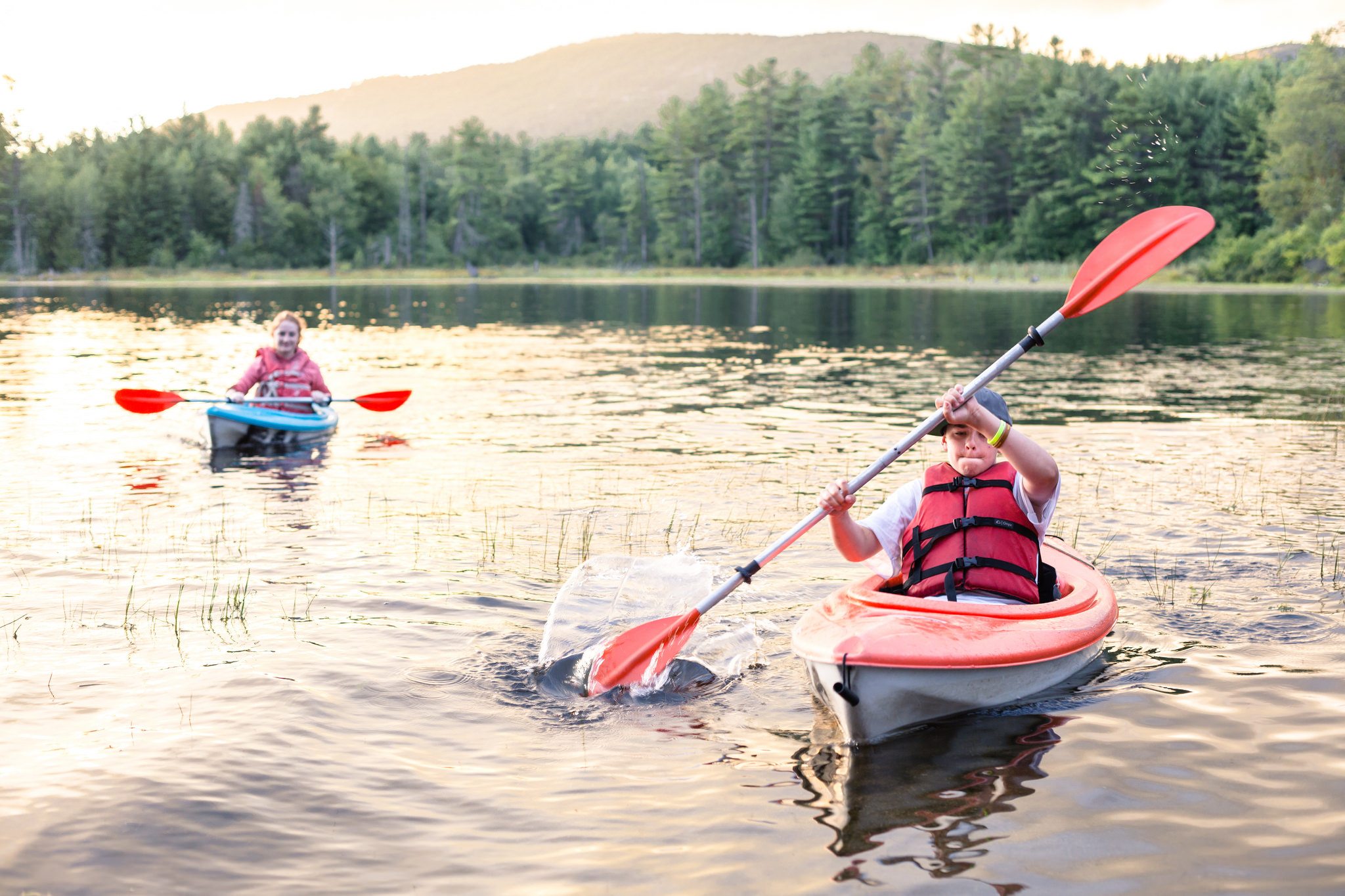 two kids kayaking on a lake.